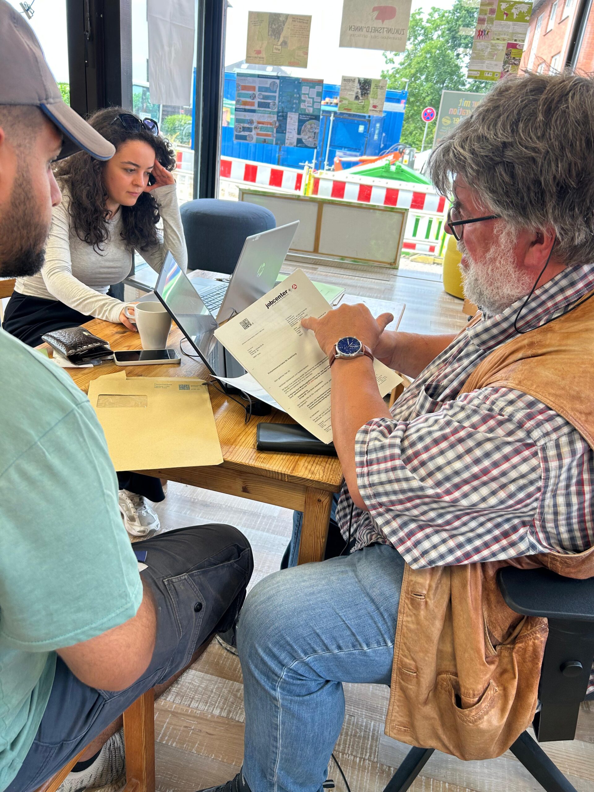 IMG-20250617-WA0021 Beratungssituation am Schreibtisch mit drei Menschen, Laptop und Papier