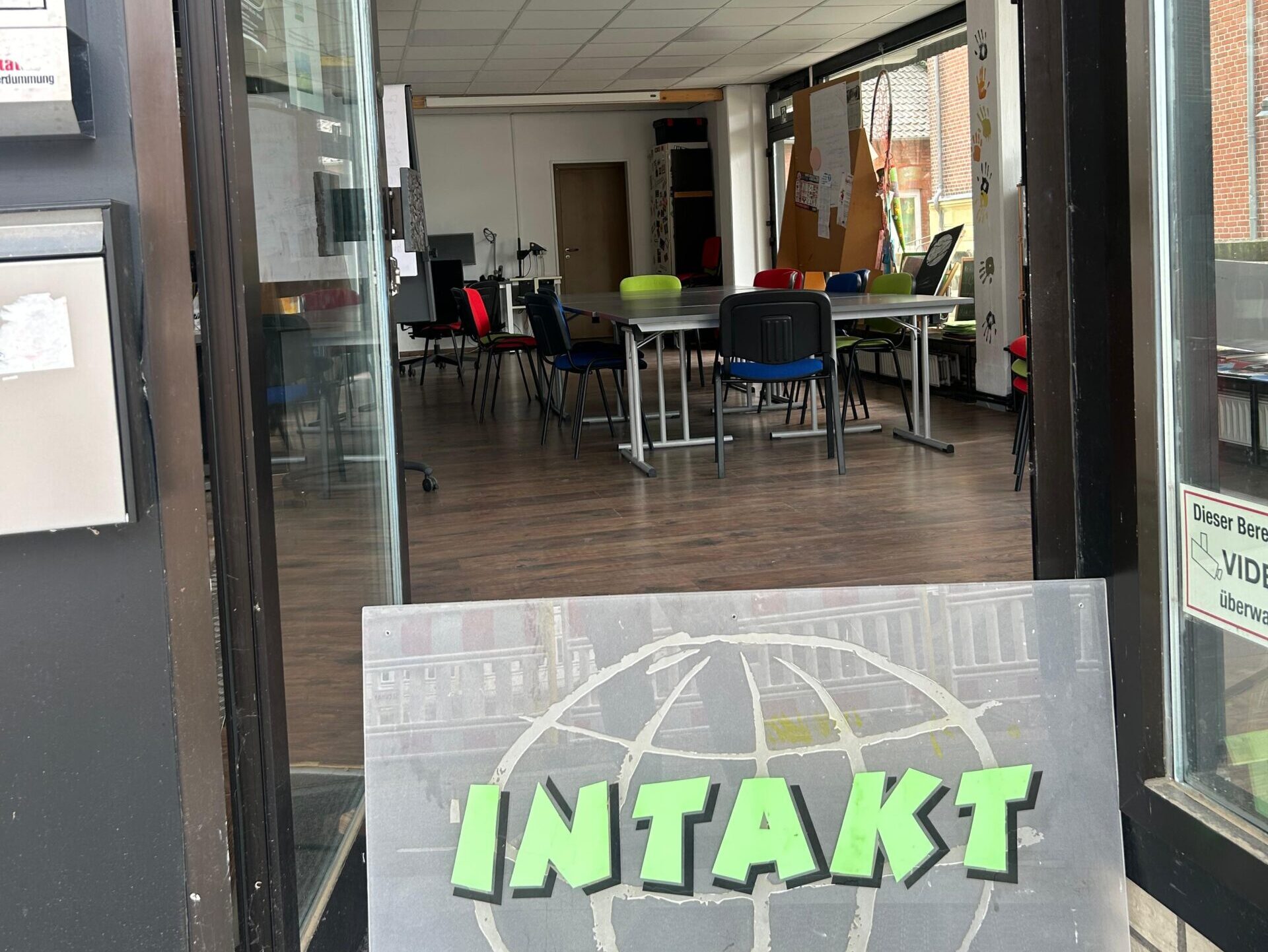 IMG-20251016-WA0065 Foto vom Eingang zu den Räumen von INTAKT mit einem Schild an der Tür und Tischen und Stühlen im Raum