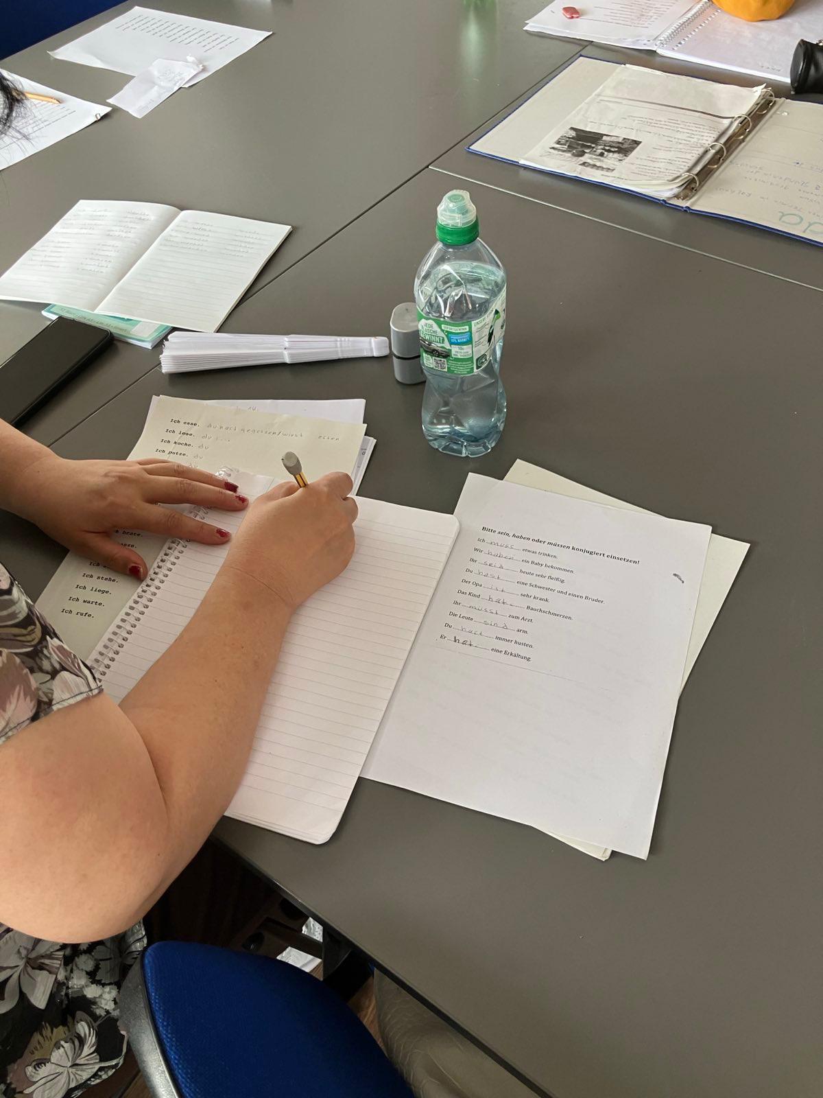 IMG-20251028-WA0020 Bein Sprachkurs sitzt eine Teilnehmende am Tisch und schreibt auf Papier
