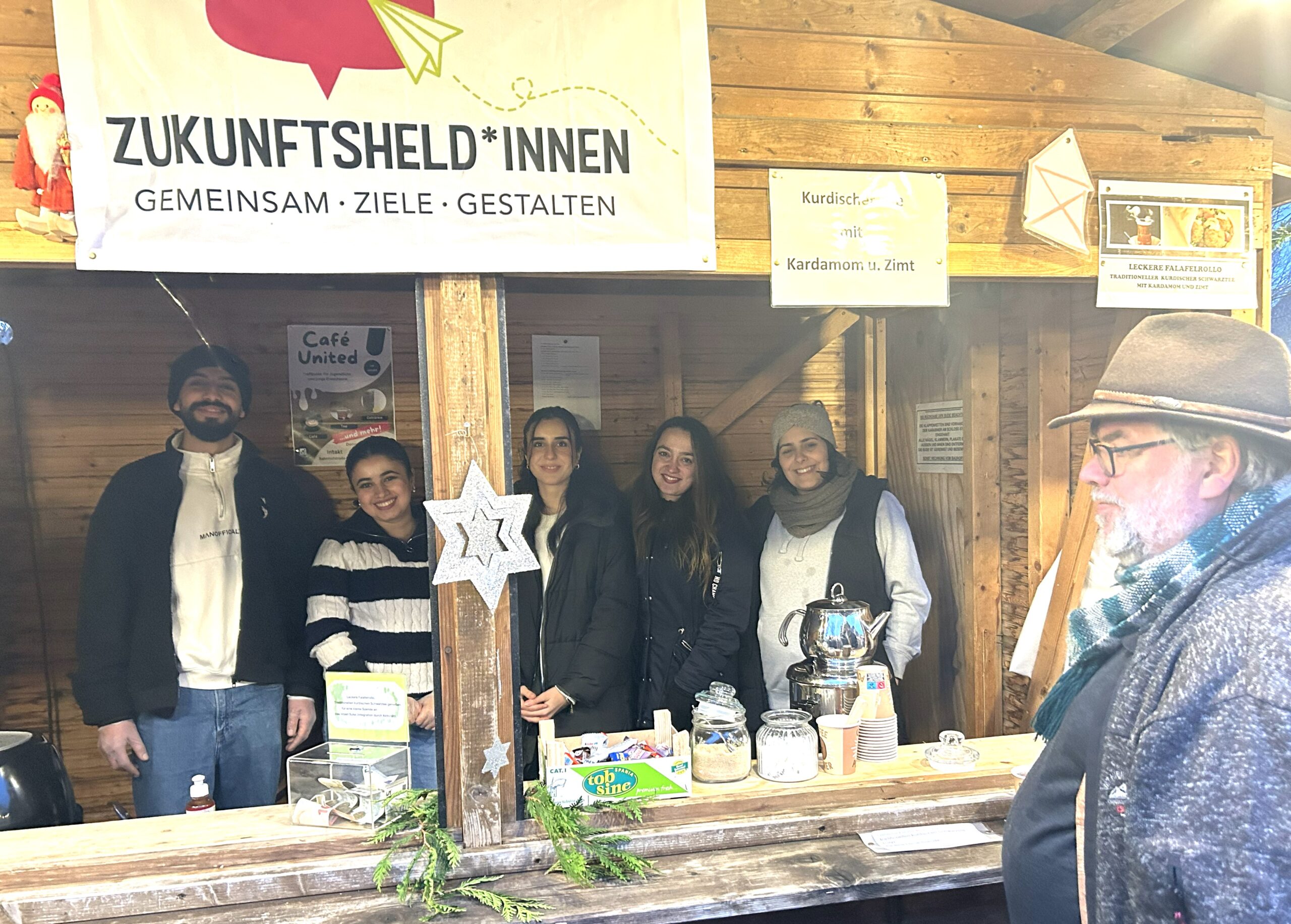 IMG_7985~photo Das Team der Jugendlichen posiert für ein Foto in einem offenen Holzhaus auf dem Weihnachtsmarkt